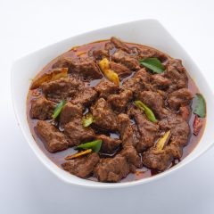 Beef masala or roast,kerala style homemade recipe garnished with coconut  pieces and curry leaves which is arranged in white bowl  with white background.