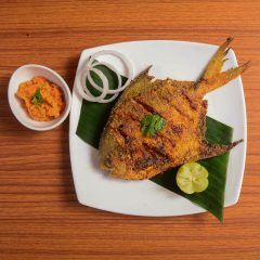 Pomfret fish tawa fry garnished with lemon and onion in a white ceramic plate with wooden background,selective focus
